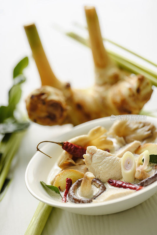 著名的国际知名泰式鸡肉配椰奶“Tom Kha Gai”，在一个碗里，连同柠檬草，卡菲莱姆叶和高隆加尔在白色的木板桌子背景上。